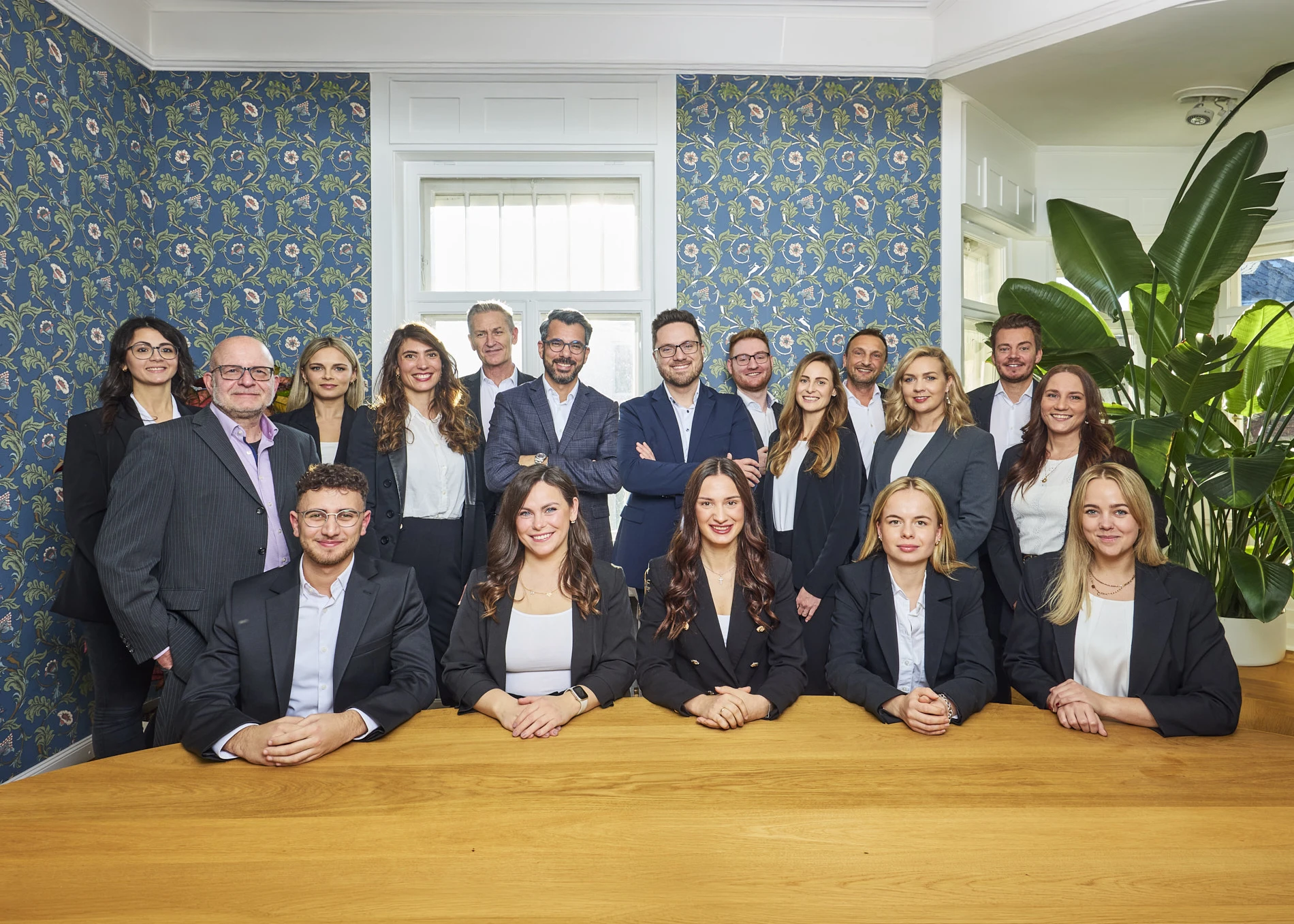 Ein Team von elf Immobilienmaklern in blauen und dunklen Anzügen posiert für ein professionelles Gruppenfoto im Fotostudio.